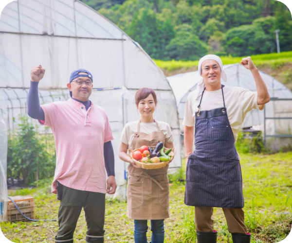 収穫した野菜を持つ笑顔の女性を中央に両隣に笑顔の男性が立っています